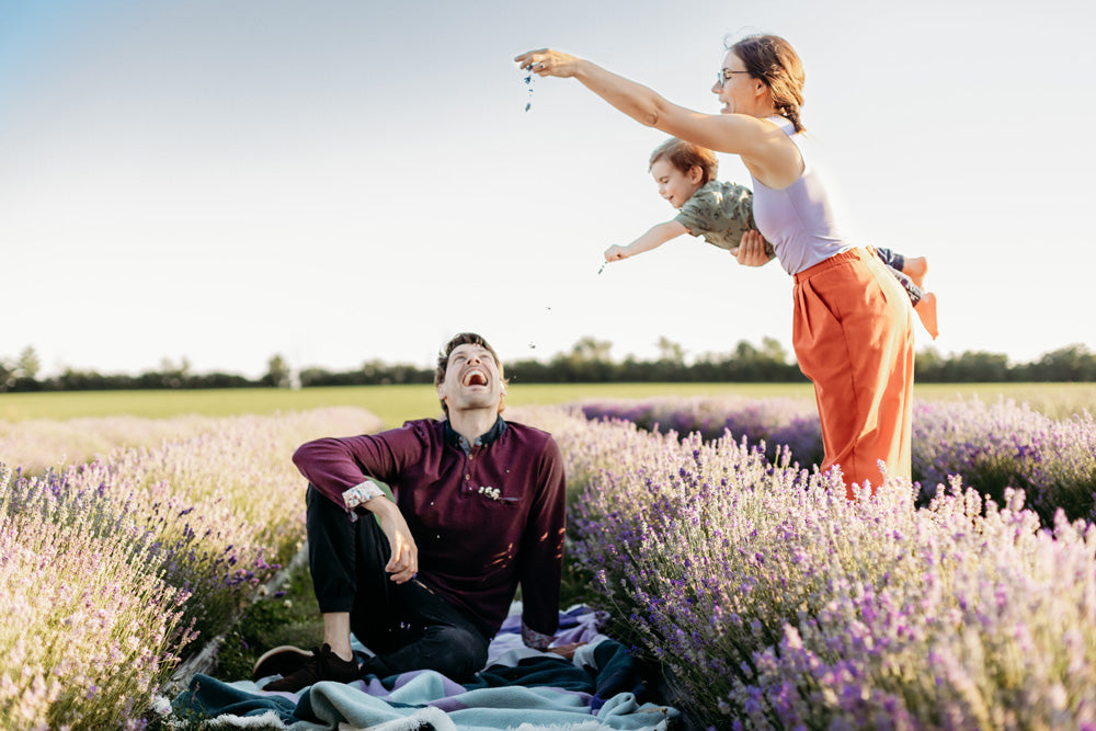 White woman and child sprinkle lavender on a man sitting in lavender field