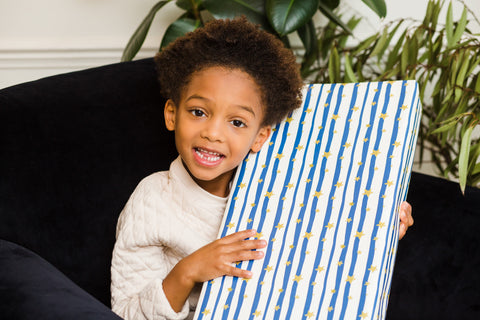 Boy sitting on sofa with box wrapped in Curlicue's stars at dusk gift wrap