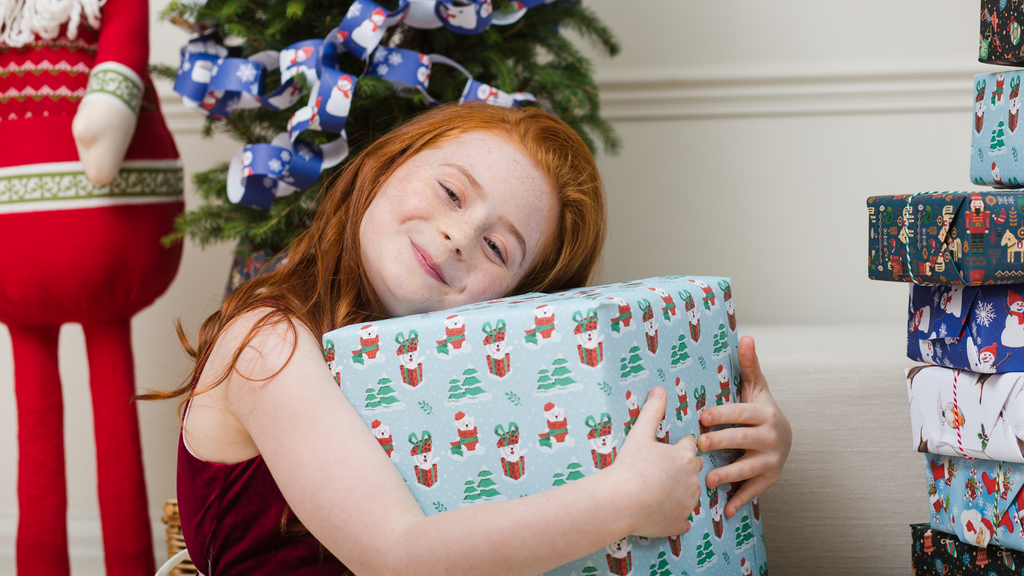 Little girl hugging a present wrapped in Pawfect Present gift wrap which features cute illustrated polar bears 