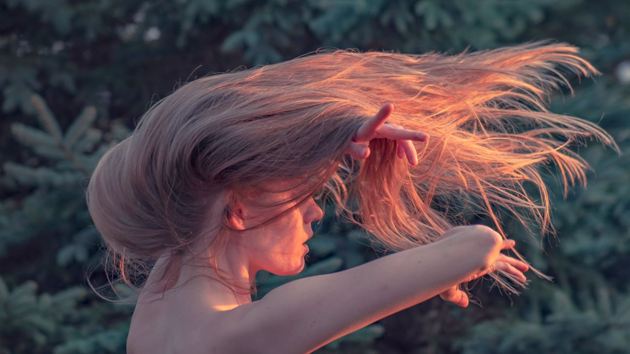 Foto de uma mulher com os cabelos ao vento e iluminada pelo sol.