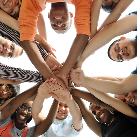 Group of people of different ethnicities holding hands in center of circular formation