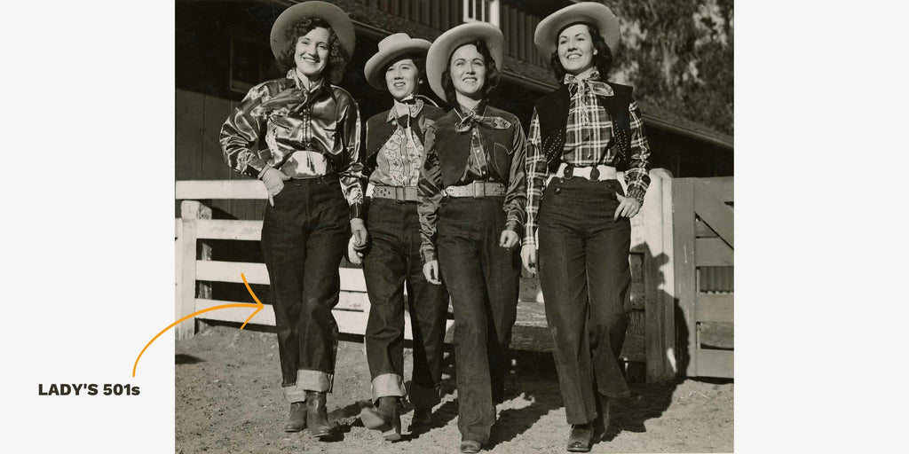 A black an white photograph of four young white women all wearing dark denim jeans, checked shirts and cowboy hats standing in a ranch.