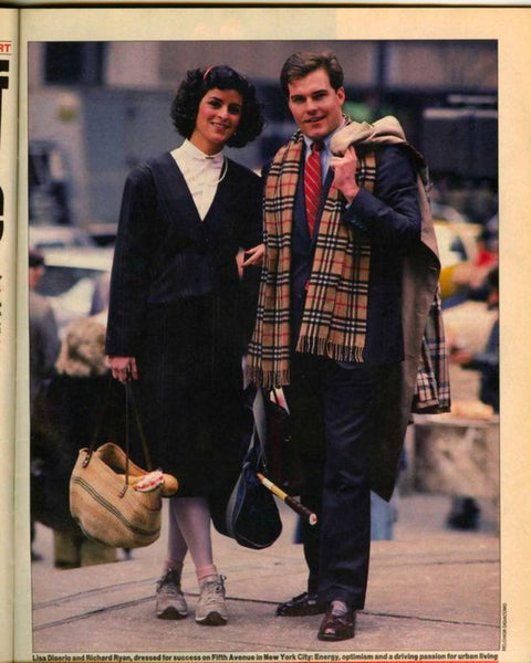 A magazine clipping of a photograph of white woman and man on the street in smart and professional 80s clothing. The man drapes a Burberry scarf around his neck.