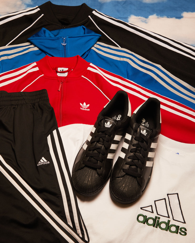 Photograph of Vintage Adidas products with the backdrop of a sky. Includes vintage adidas track jackets, vintage adidas tracksuits, vintage adidas trainers and vintage adidas t-shirt. 