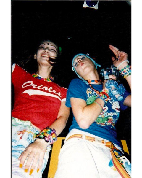 Photograph of two white women dancing in a 90s rave, wearing cropped tees and 90s baggy trousers.