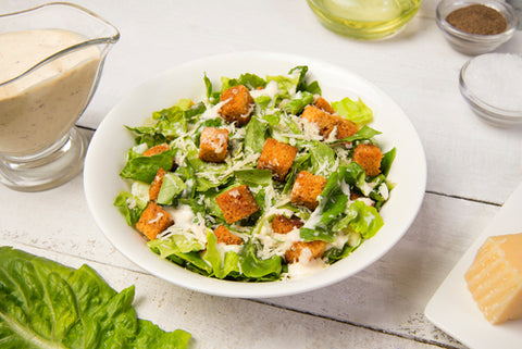 A caesar salad surrounded by lettuce, and extra sauce. Enjoy a healthy salad packed with nutrients, that is cruelty-free.
