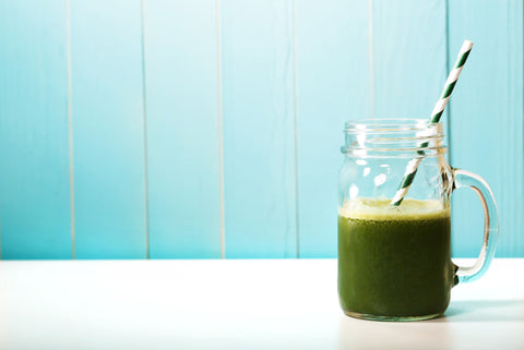 A green juice in a jam jar cup, against a blue background. Choose from our selection of the best sea moss drink recipes!