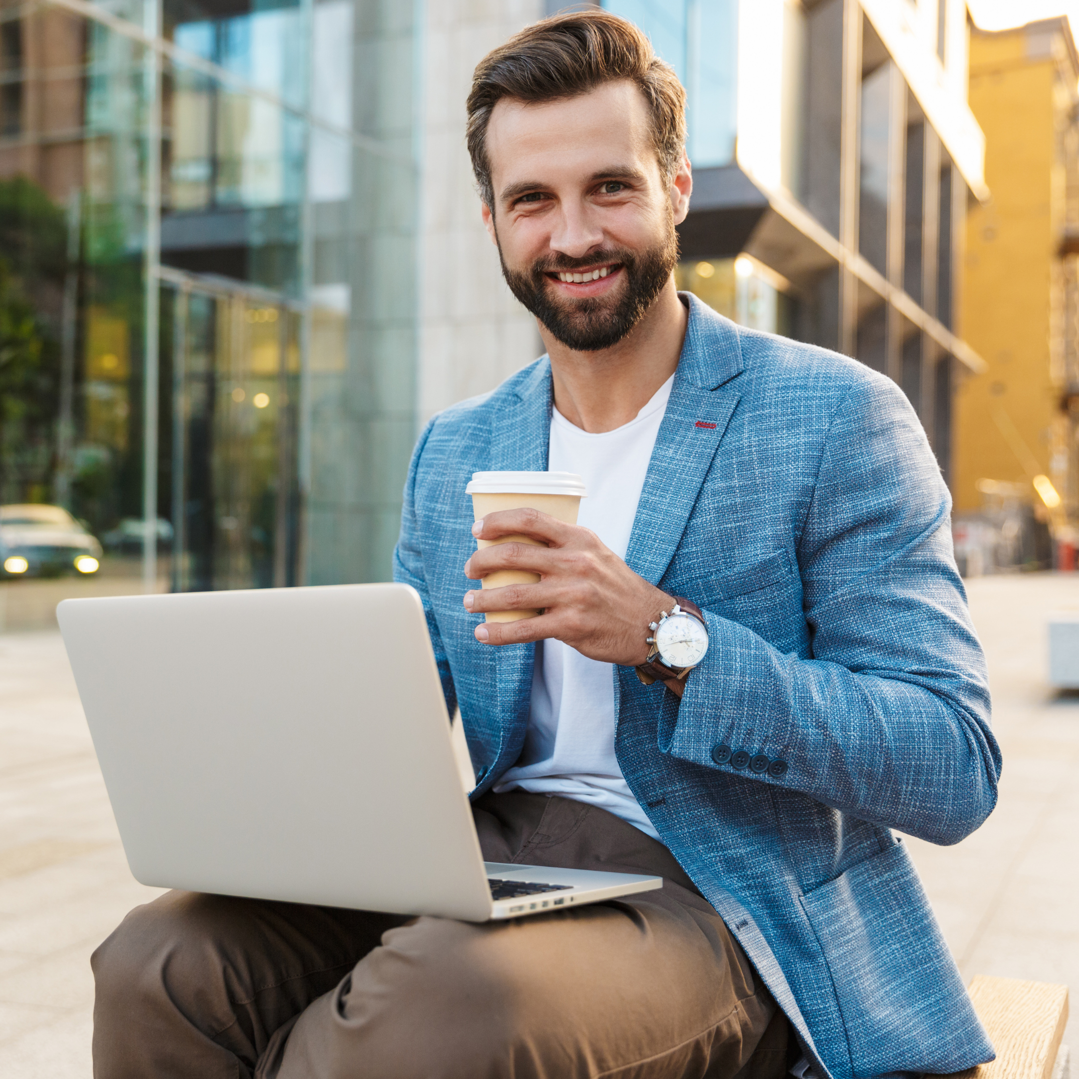 Man sitting outside while using laptop and enjoying cup of coffee