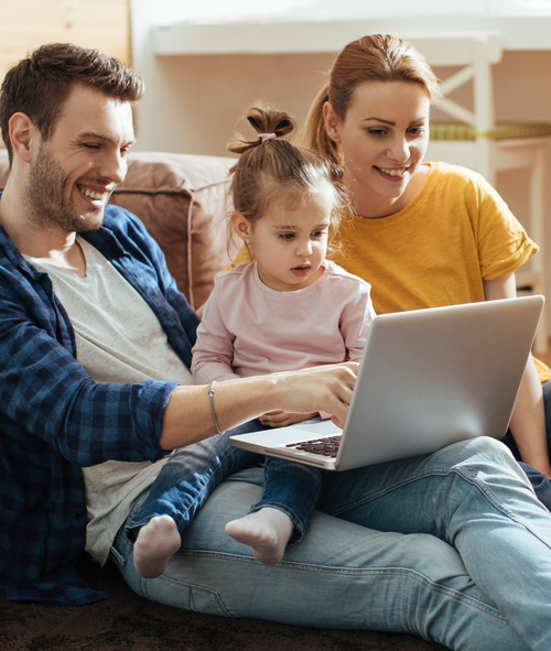 Mom, dad and young daughter viewing laptop screen while sitting on the couch