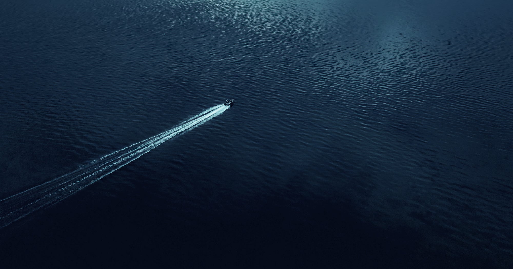 A small boat glides across the lake at high speed, seen from above.
