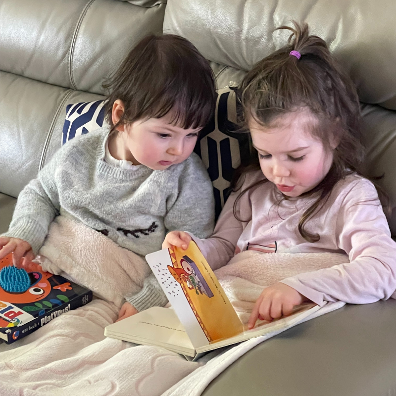 Gigi and Lena reading a book on the couch together