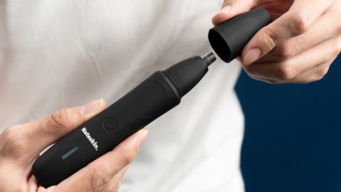 Person's hands holding and operating a Nateskin nose hair trimmer, demonstrating how to attach the head onto the device.