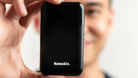 Smiling person holding a compact Nateskin shaver in front of them, showcasing its small size and portability.