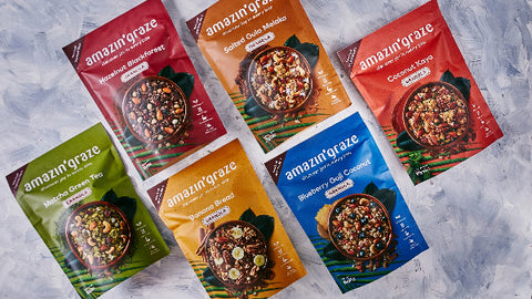 Image of a variety of Amazin' Graze granola packets spread out on a textured surface, showcasing different flavors for healthy snacking options.