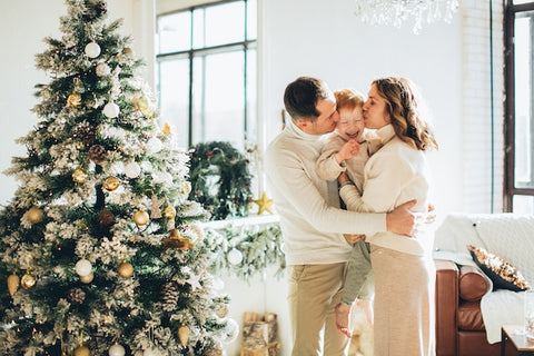 Mum and Dad kiss their son next to a large Christmas tree