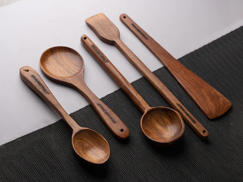 Four wooden ladle of varying sizes on a dark grey mat against a white backdrop.