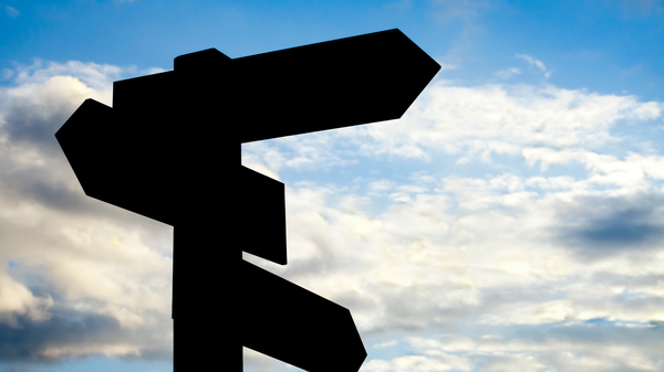 A signpost with several arrows pointing in different directions is silhouetted against the sky.