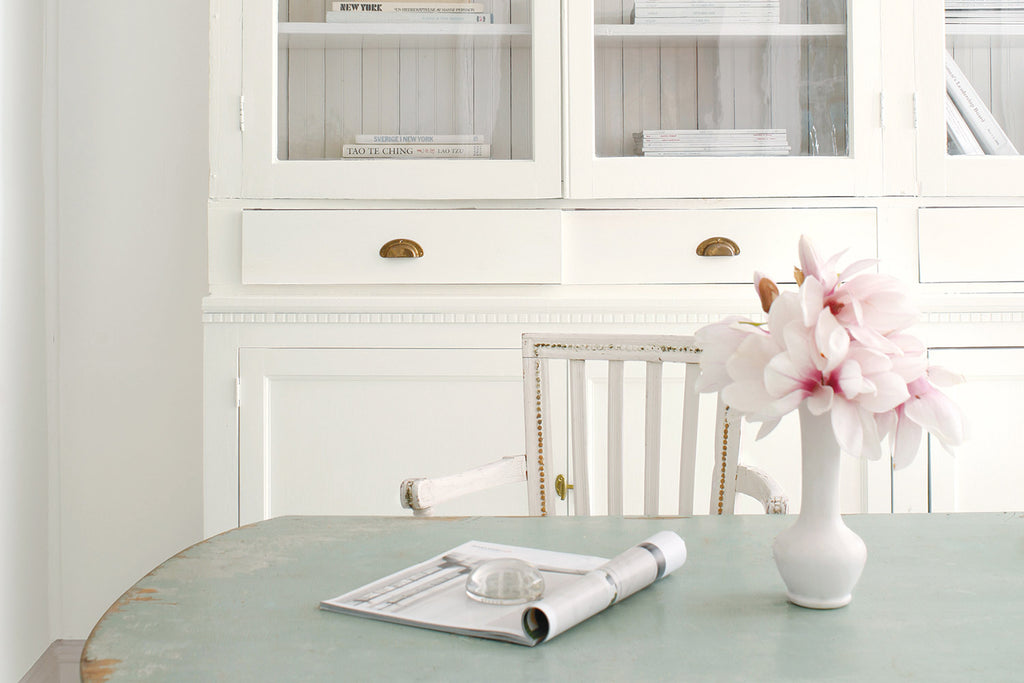 rustic painted dining table with flower vase in front of white painted cabinet