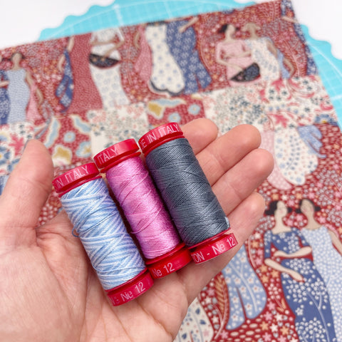 Sarah holding three embroidery threads in her hand, a blue, a pink and a dark grey