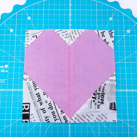 Completed heart block with pink/purple centre and newspaper fabric background 