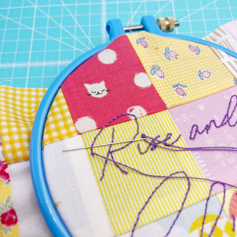 Hand stitching of the words 'Rise and Shine' in purple thread 