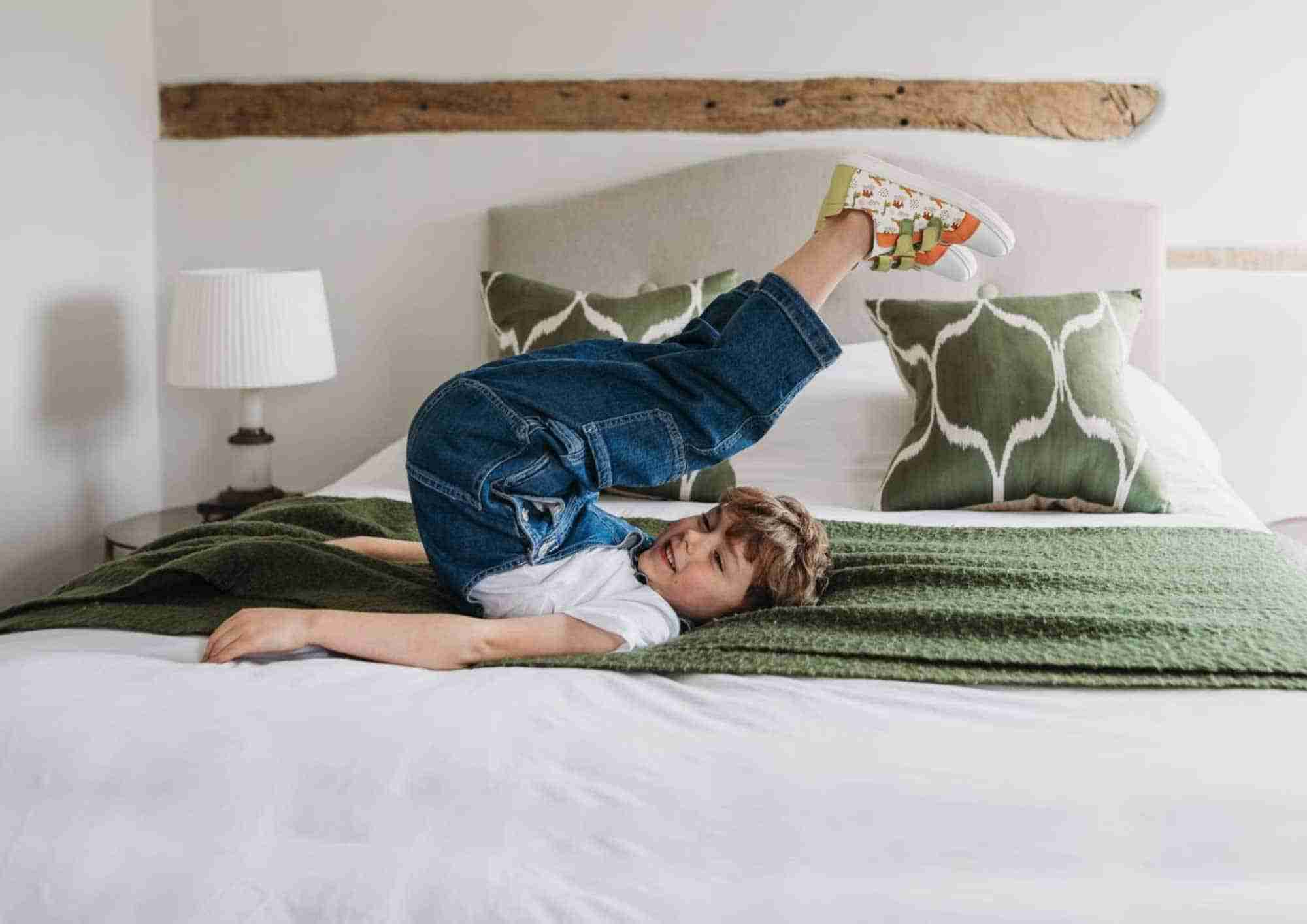 Little boy laying on bed wearing Pip and Henry Sustainable sneakers