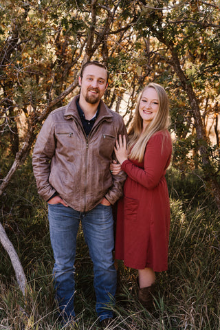 a man and woman posing for a professional photo in front of some trees