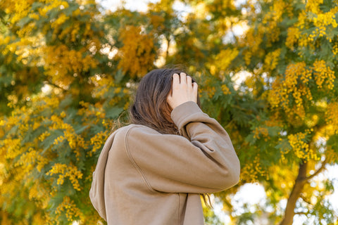 Photo of woman holding her head and standing in front of yellow flowers.