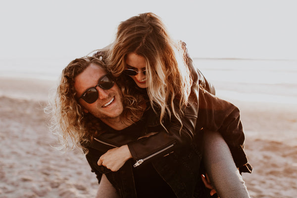 Man giving a woman a piggy back on the beach, both wearing sunglasses