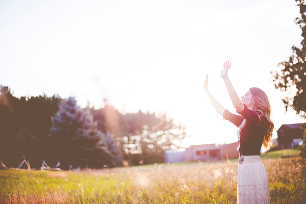 woman with arms raised standing in a sunny field