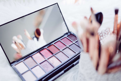 A cream eyeshadow palette with pot of makeup brushes.