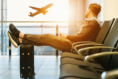 man waiting with a suitcase at an airport whilst a plane takes off in the background