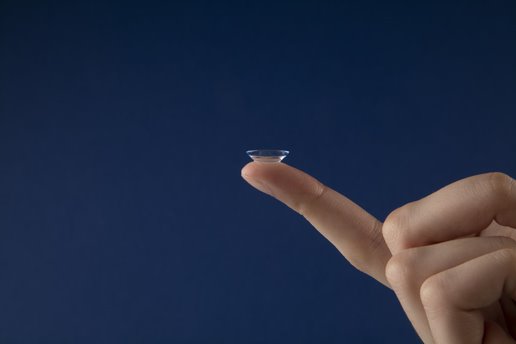 contact lens balancing on the tip of a finger against a blue background