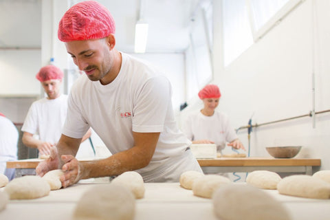 Ein Bäcker beim Formen von Brotlaiben. Auf dem weißen T-Shirt das rote Logo der Firma Hack.