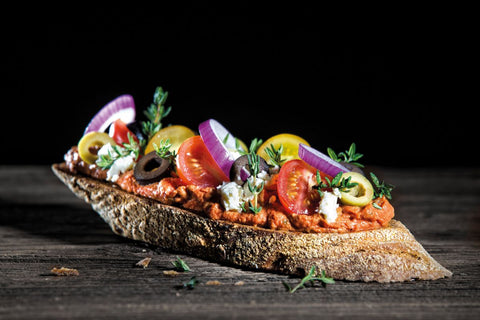 Bild eines gesunden Snacks: Knuspriges Brot mit Tomaten, Zwiebeln, Oliven und mehr.