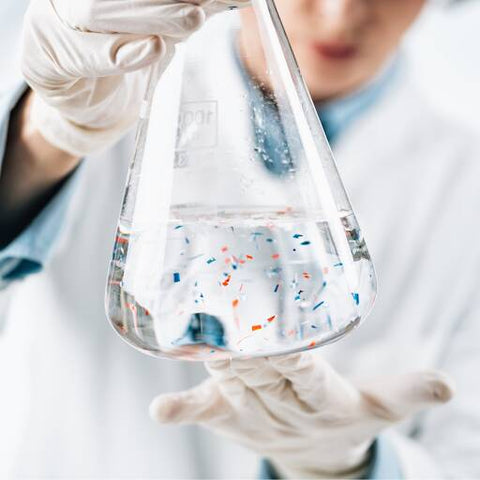 Scientist holds a beaker full of microplastics in a solution
