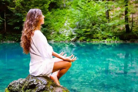A woman meditates in lotus position near the water