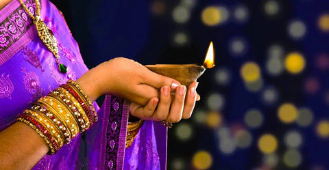 Indian woman dressed in purple and gold holds lit clay lamp during the Indian festival of lights