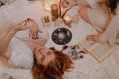 Two women perform full moon rituals with books and candles