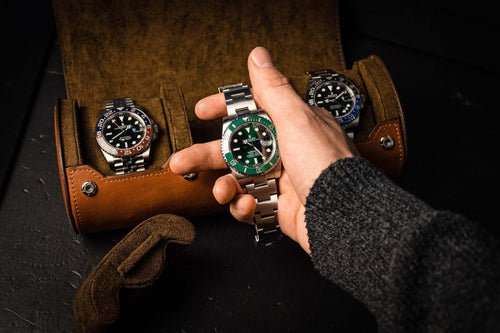 An image showing Luxury Watch Rolls vintage brown leather triple slot watch roll, for three watch storage. The case is open and a Rolex Submariner Hulk is shown being held about to be placed on a watch pillow. The Rolex GMT Master II Pepsi is shown stored in the case. 