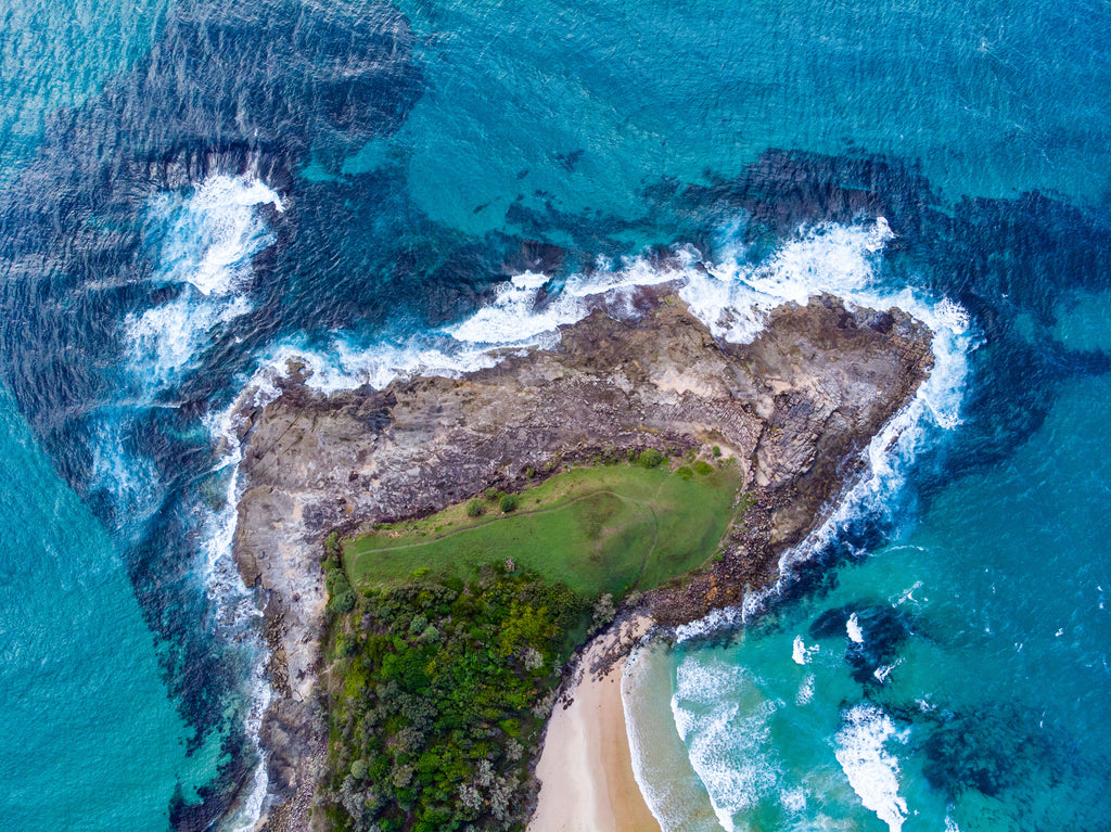 A beach with a green park in the middle next to a blue sea in Yamba