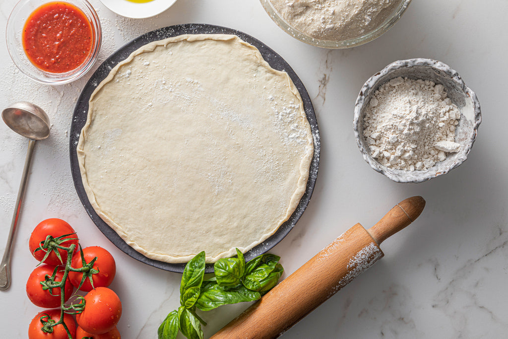 Pizza base with sauce, herbs and flour surrounding it