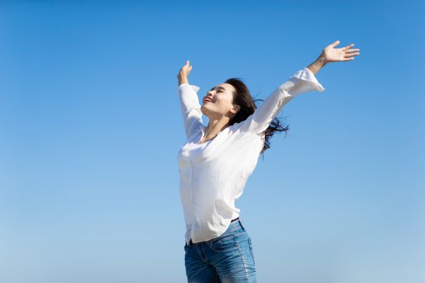 気持ちよさそうに青空に向かって手を広げる女性