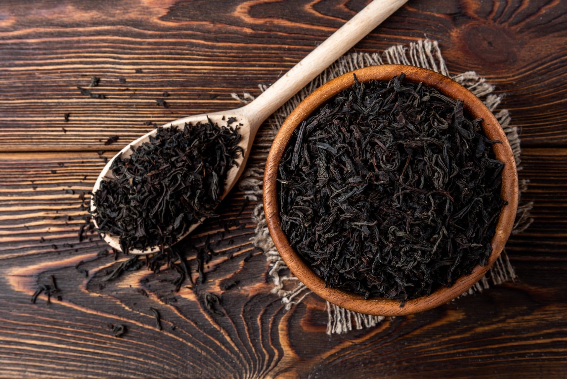 Loose leaf black tea in a wooden spoon and in a small bowl that sit next to each other on a wooden table