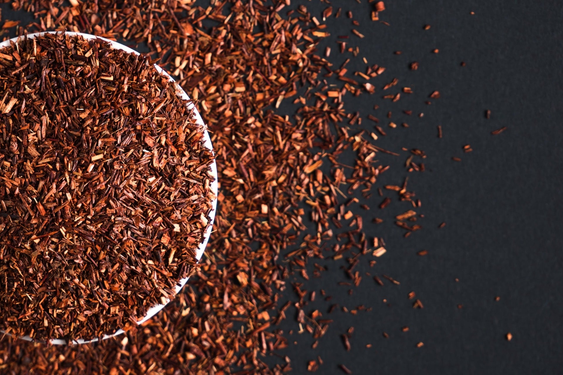 Loose leaf Red Rooibos tea that has overflowed from a bowl onto a table in an artistic image.