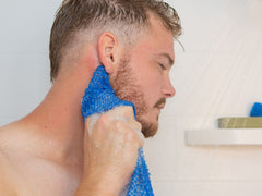 man scrubbing behind ear with finger wrapped around WOWO exfoliating mesh body scrubber