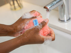 woman's hands agitate WOWO mesh exfoliating scrubber in a sink and forms lather