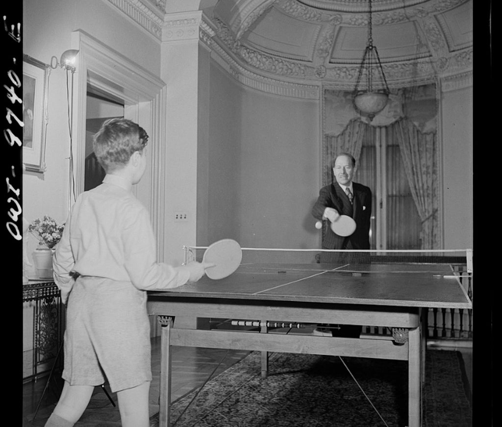 Young boy playing table tennis in the 19th century inside a fancy mansion with presumably his butler.