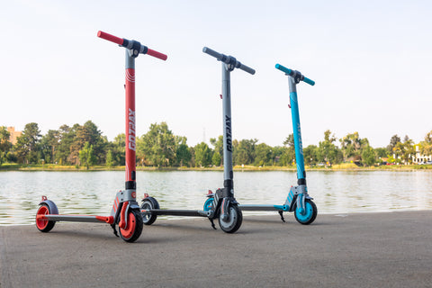 A Red, Gray, and Ocean Teal GOTRAX Vibe Electric Scooters for Teens at a park