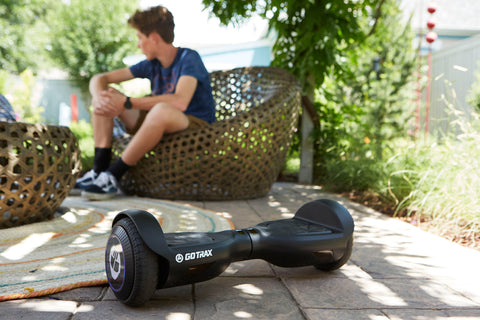 Child sitting next to a GOTRAX Black Edge Self-Balancing Hoverboard 6.5"